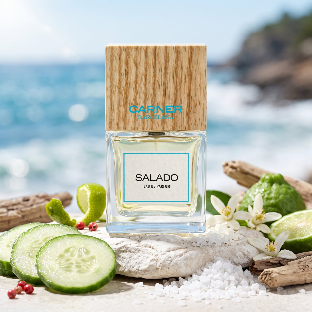 Frasco de cristal con líquido amarillo claro, etiqueta blanca con borde azul turquesa y tapón de madera natural de Salado de Carner Barcelona, rodeado de pepino, sal marina, flor de azahar y maderas, estilo Casa Flores.