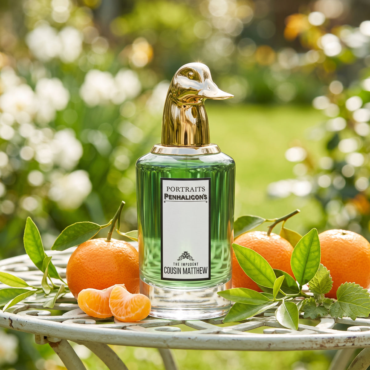 Frasco cilíndrico con líquido verde claro, etiqueta vertical blanca y tapón dorado con forma de cabeza de pato de The Impudent Cousin Matthew de Penhaligon's, rodeado de mandarina, petit grain y pachulí, estilo Casa Flores.