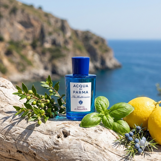 Frasco azul del perfume Acqua di Parma Mirto di Panarea rodeado de ramitas de mirto, albahaca fresca y cítricos con el mar Mediterráneo de fondo.