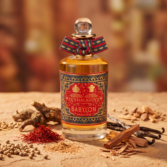 Frasco de Babylon de Penhaligon's con lazo rojo y etiqueta ornamental, rodeado de azafrán, vainilla y maderas, estilo Casa Flores.