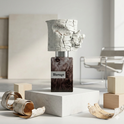 Frasco de Nasomatto Blamage sobre un pedestal de madera clara en un estudio de arte minimalista y moderno, rodeado de fragmentos de madera blanca y lienzos en blanco.