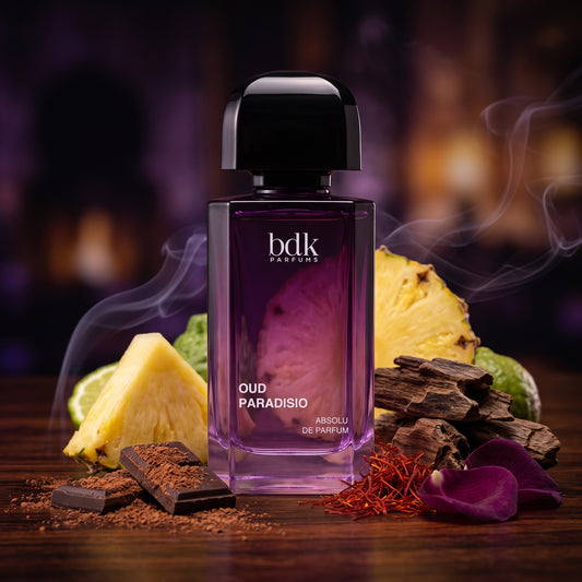 Frasco morado oscuro de Oud Paradisio de BDK Parfums con tapón negro sobre madera oscura con piña, rosas y madera de oud, estilo Casa Flores.