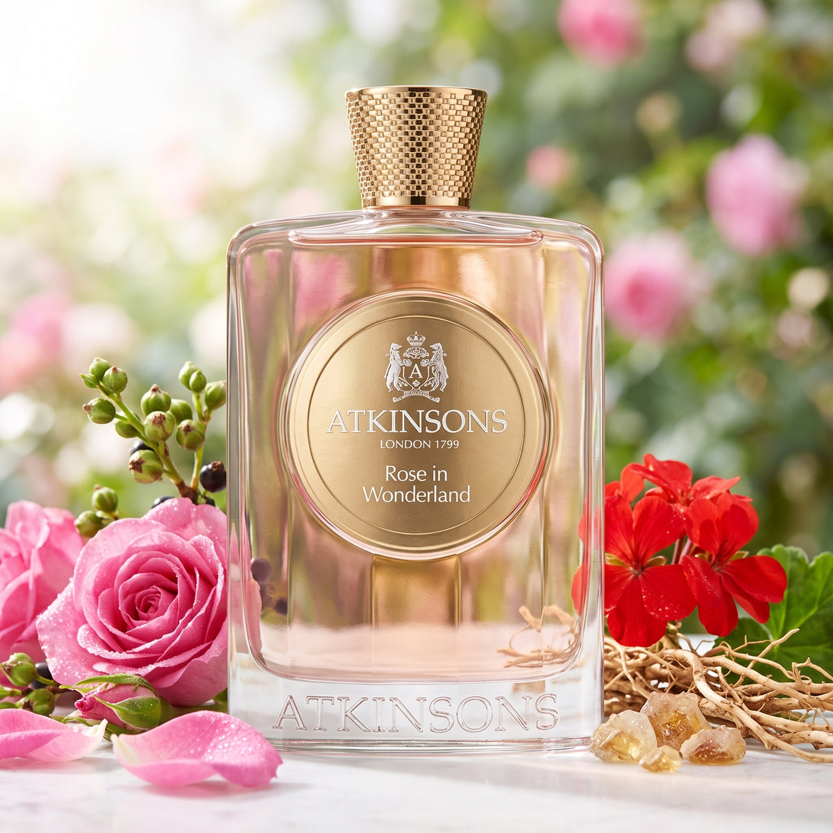 Frasco transparente con líquido rosado, placa y tapón dorado de Rose in Wonderland de Atkinsons, rodeado de rosas, geranio y vetiver, estilo Casa Flores.