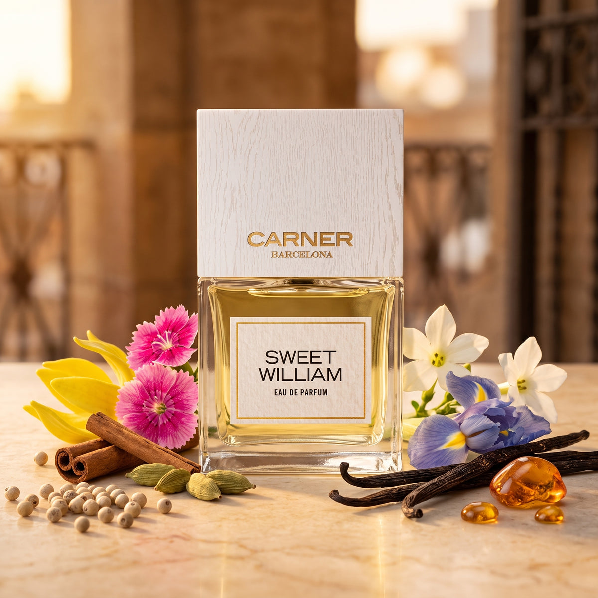 Frasco de cristal con líquido amarillo pálido, etiqueta blanca con borde dorado y tapón de madera blanca de Sweet William de Carner Barcelona, rodeado de clavel, pimienta, vainilla e iris, estilo Casa Flores.