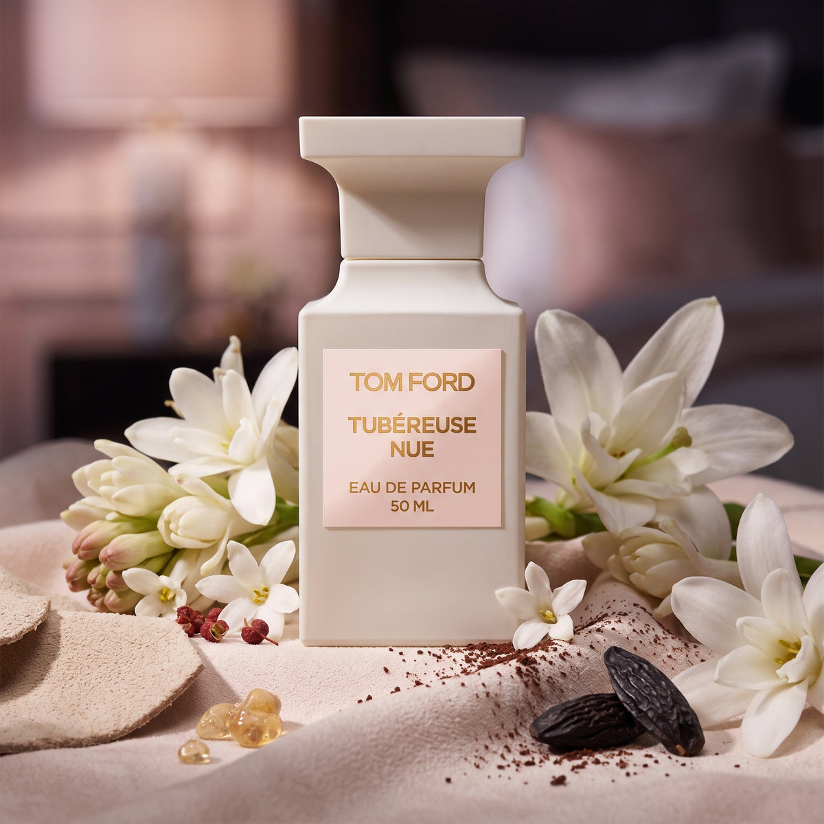 Frasco arquitectónico blanco marfil mate con etiqueta rosa pálido y letras doradas de Tubéreuse Nue de Tom Ford, rodeado de nardos, jazmín, gamuza y cacao, estilo Casa Flores.